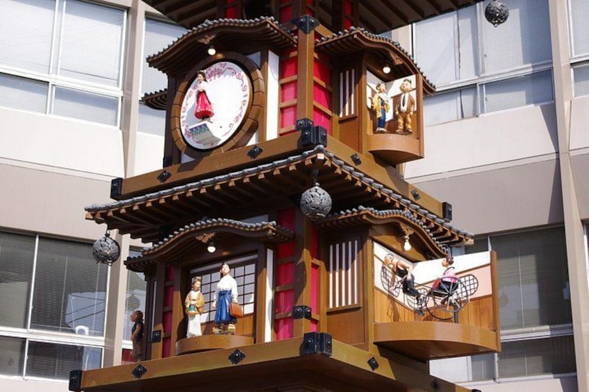 A wooden clock tower with figures, a bicycle, and a building in the background. 2