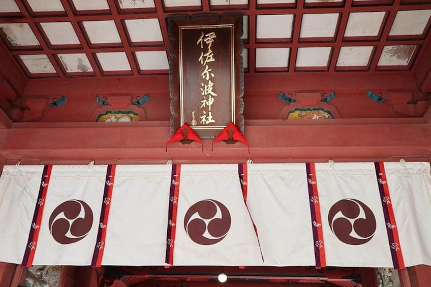 A traditional Japanese building with a red wooden ceiling and white walls. There are banners with a circular emblem hanging from the ceiling. 4