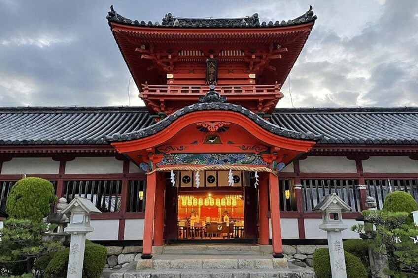 A traditional Japanese temple with a red roof, white walls, and a stone lantern in the foreground. 3