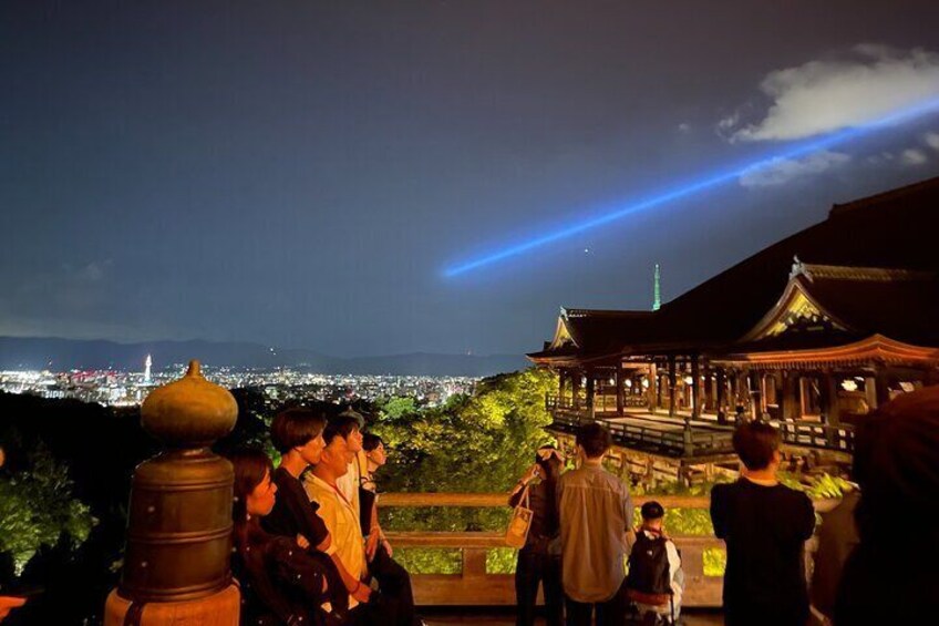 A group of people observing a traditional building at night with a cityscape in the background. 5