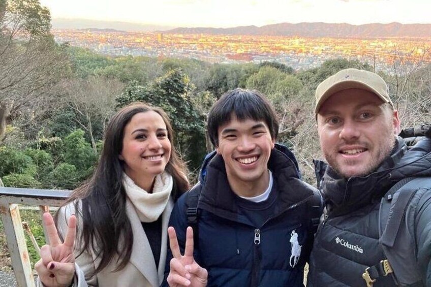 Three people posing with peace signs in a mountainous area with a city in the background. 2