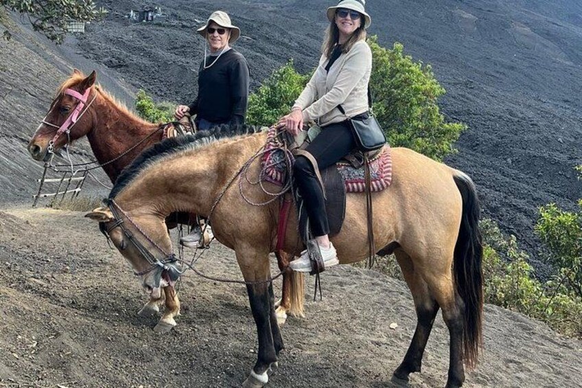 Två personer som rider på hästar på en sluttning, med ett vulkaniskt landskap i bakgrunden. 4
