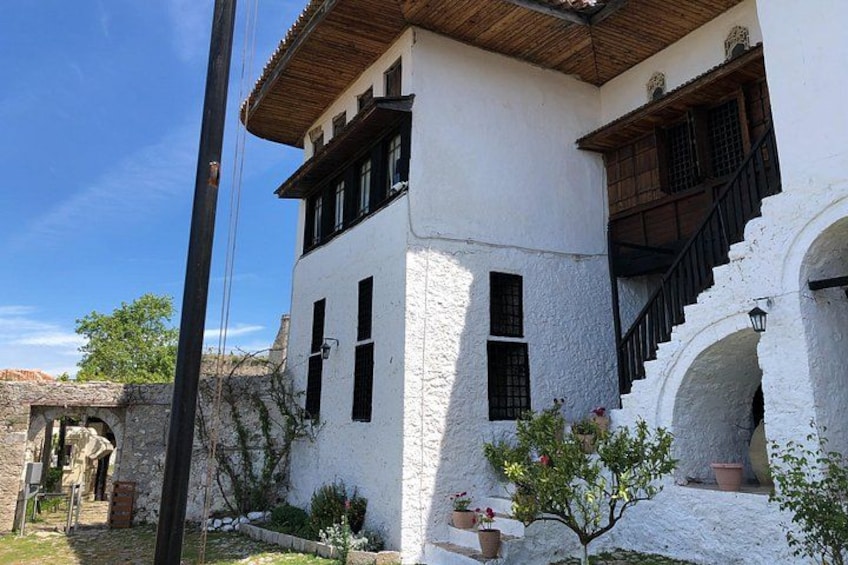 A white building with a wooden roof, black shutters, and a staircase leading to an upper level. 1