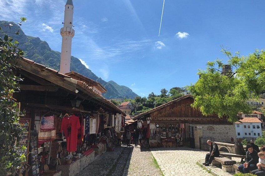 A narrow street with shops, a mosque, and mountains in the background. 1