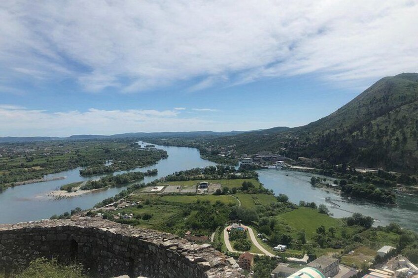 A river winding through a valley with a bridge, green hills, and a stone structure. 5