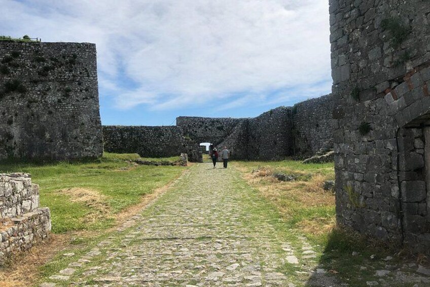 A stone pathway leading through ancient ruins with stone walls and a clear sky. 3