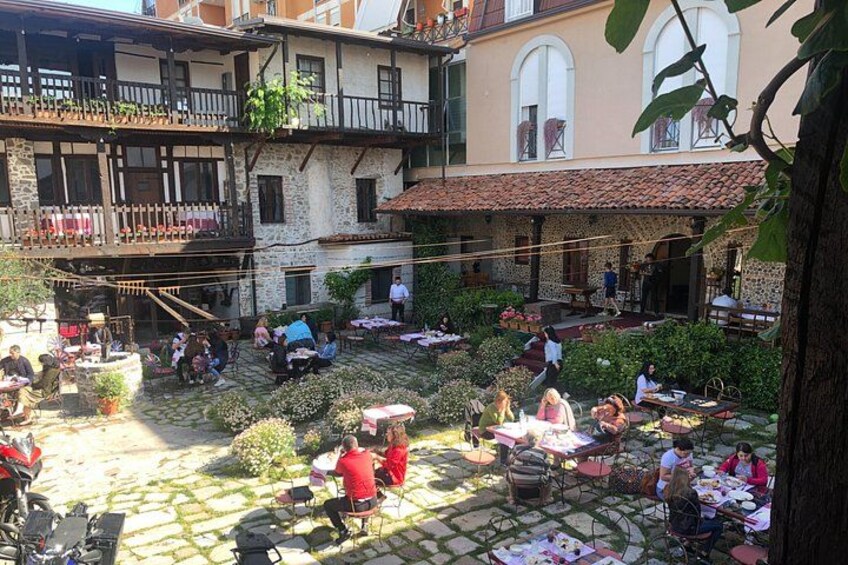 A courtyard with people sitting at tables, surrounded by buildings with balconies and plants. 2