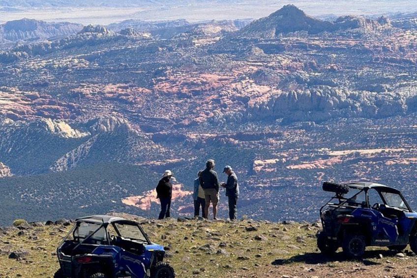 Three people standing on a mountain top with a view of a valley below. There are two ATVs parked in the foreground. 5