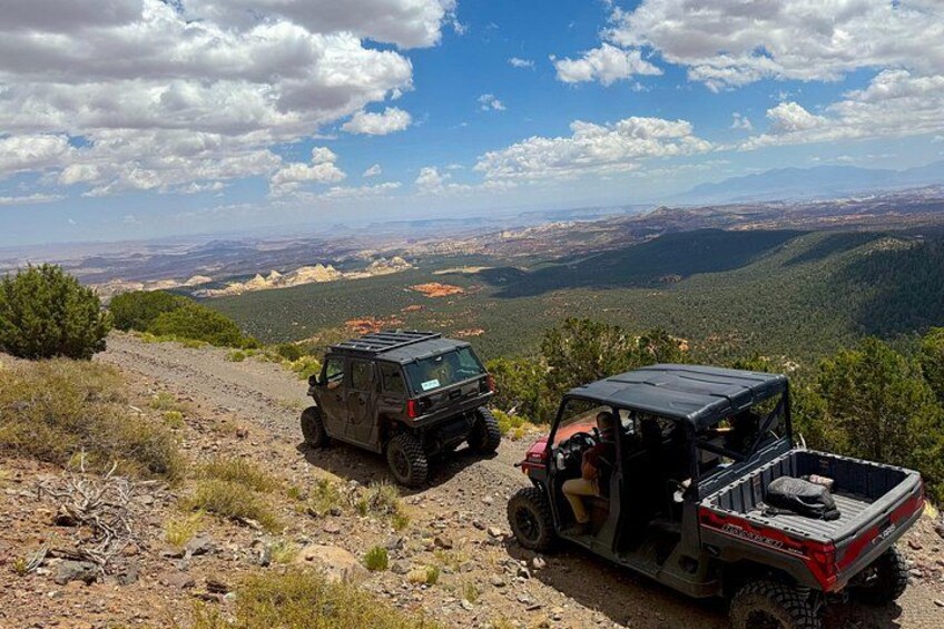 Two off-road vehicles on a dirt path with a mountainous landscape in the background. 1