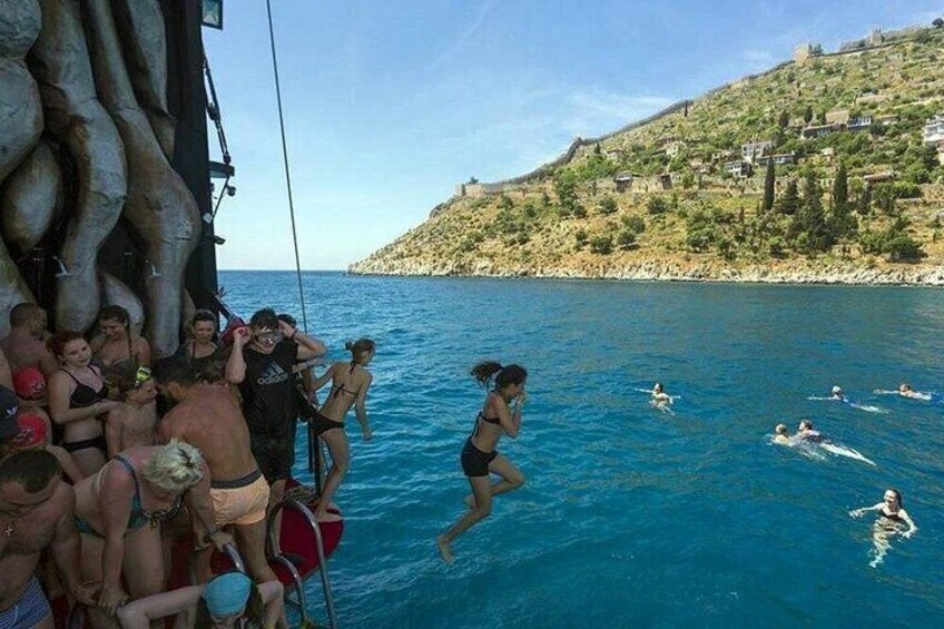 People swimming in the sea, a boat, and a hill with houses. 2