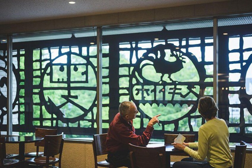 Two people sitting at a table with a large window behind them, featuring a decorative design with a circular pattern and Chinese characters. 2