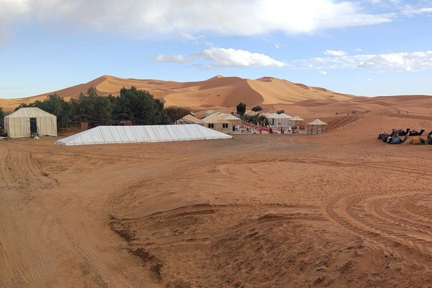 A desert landscape with sand dunes, tents, and camels. 1