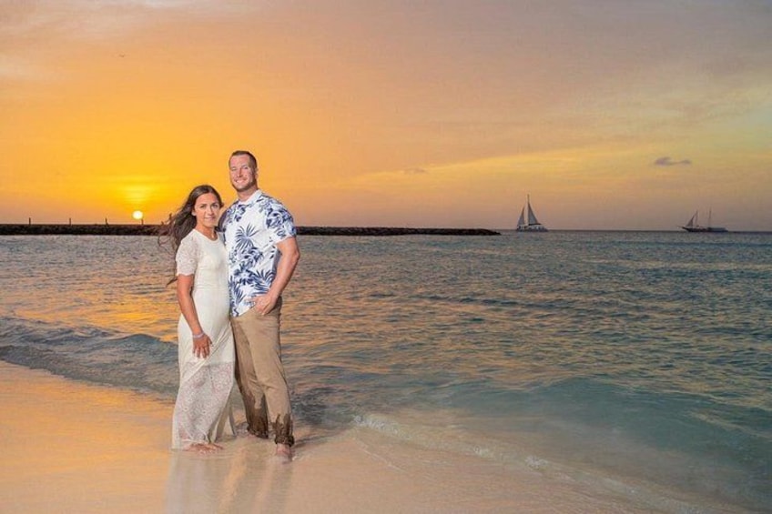 Una pareja está de pie en una playa con un atardecer de fondo y veleros en el agua. 3