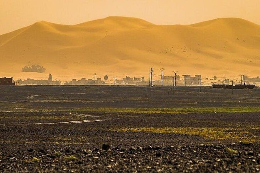 A desert landscape with sand dunes, a road, and distant buildings. 2