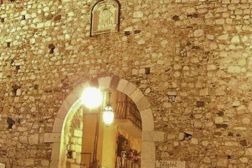 A stone wall with an arched doorway and a hanging light fixture. 3
