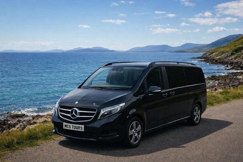 Una furgoneta negra Mercedes-Benz estacionada en una carretera costera, con una vista panorámica del mar y las montañas al fondo. 2