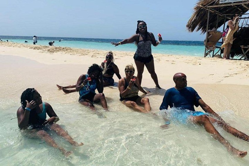 People on a beach with clear water and a thatched structure in the background. 3