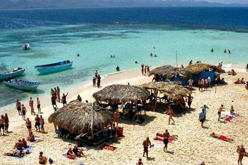 Une plage avec des gens, des bateaux et des constructions à toits de chaume. 1