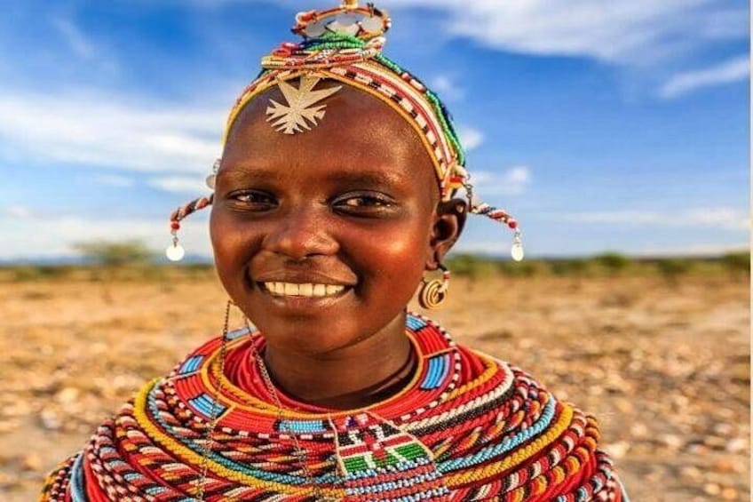 Une personne vêtue d’un costume traditionnel aux couleurs vives, orné de motifs complexes en perles, se tient dans un paysage aride et dégagé. 4
