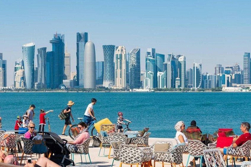 Un paseo marítimo con gente descansando en sillas, un horizonte urbano al fondo y un cielo azul despejado. 4