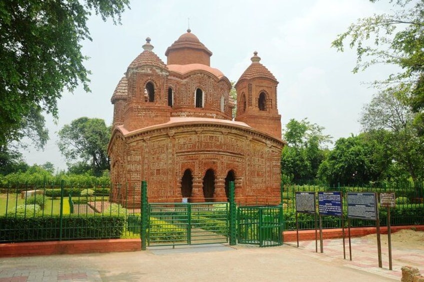A historic brick building with domes and arches, surrounded by a green fence and trees. 2