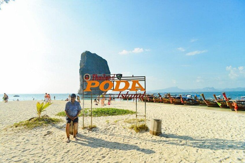 Una playa con un letrero que dice 'Thailand Poda', una gran formación rocosa y una fila de botes. 4