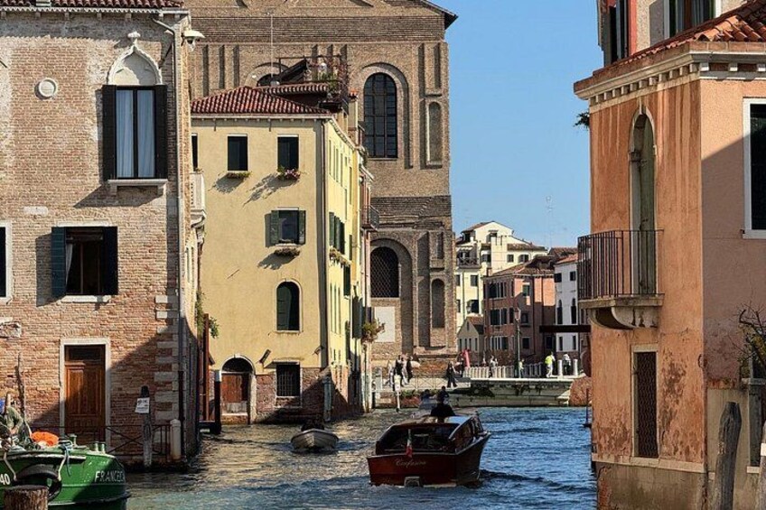 A narrow Venetian canal with boats, historic buildings, and a clear sky. 2