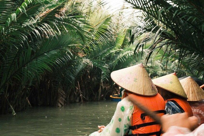 Persone su una barca indossano caratteristici cappelli a forma di cono, immerse in una fitta vegetazione tropicale. 1
