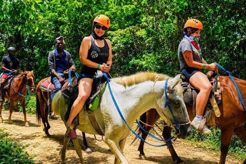 Personas montando a caballo por un sendero de tierra rodeado de vegetación. 2