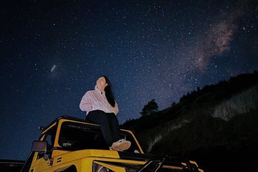 A person sitting on a yellow vehicle under a starry night sky with the Milky Way visible. 5