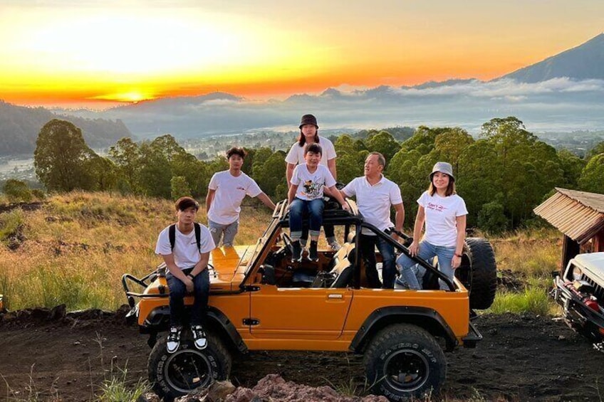 A group of people on a yellow off-road vehicle in a grassy area with a sunset in the background. 1