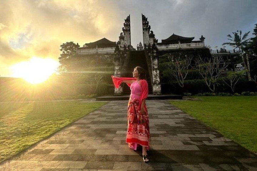 Una persona con un vestido rosa de pie frente a una puerta tradicional, con un atardecer de fondo. 2