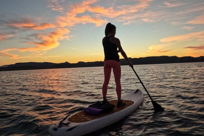 A person paddleboarding on a calm body of water during sunset. 1