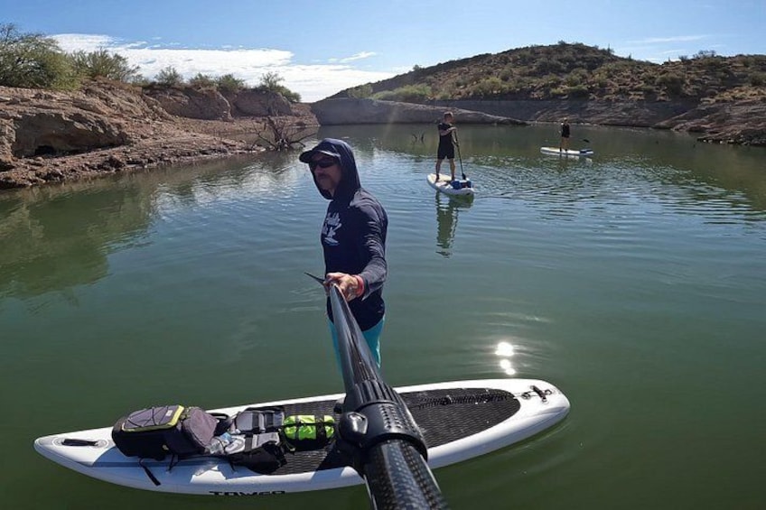 A person paddleboarding on a calm river with another person in the background. 3