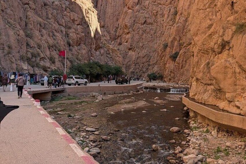 A rocky canyon with a small stream, a paved walkway, and people walking. 4
