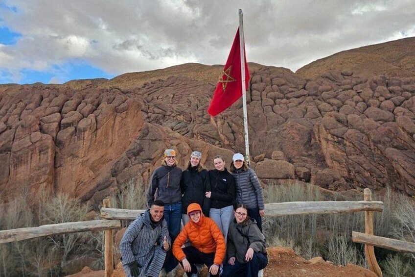 A group of people posing in front of a rocky landscape with a flag. 1