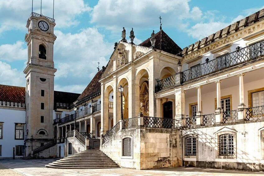 Un edificio histórico con una torre de reloj, una escalera que conduce a la entrada y un balcón con barandillas de hierro forjado. 2