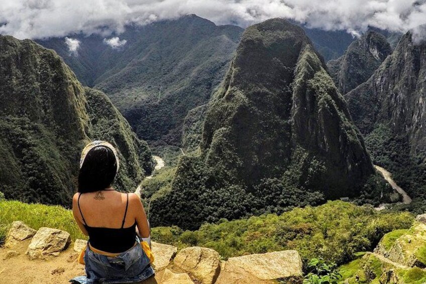 Una persona sentada sobre una roca contemplando un paisaje montañoso con una carretera sinuosa. 5