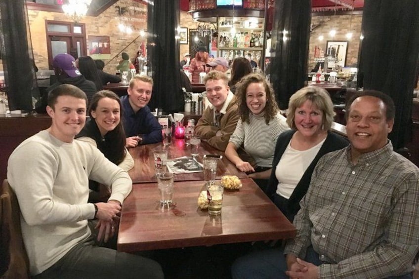A group of people seated at a wooden table in a restaurant with a bar in the background. 5