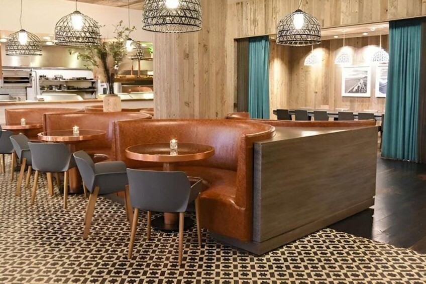 A restaurant interior with wooden panel walls, leather booths, and round tables. 3