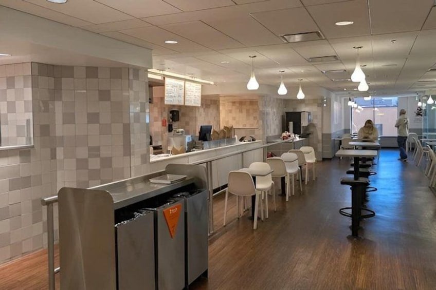 A modern cafeteria with a long counter, white chairs, and hanging pendant lights. 2