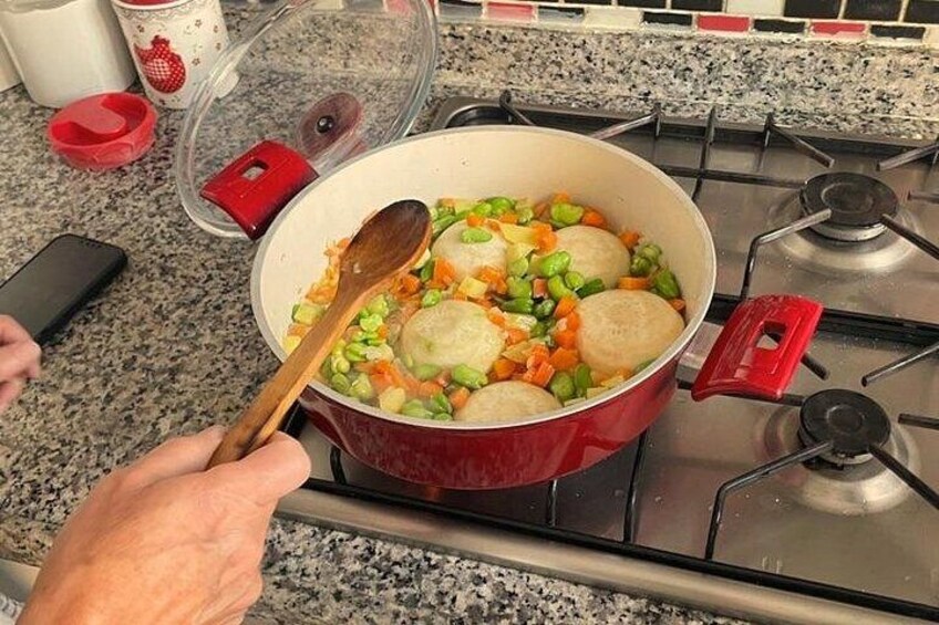 A red pot on a stove with vegetables and dumplings being cooked. 5