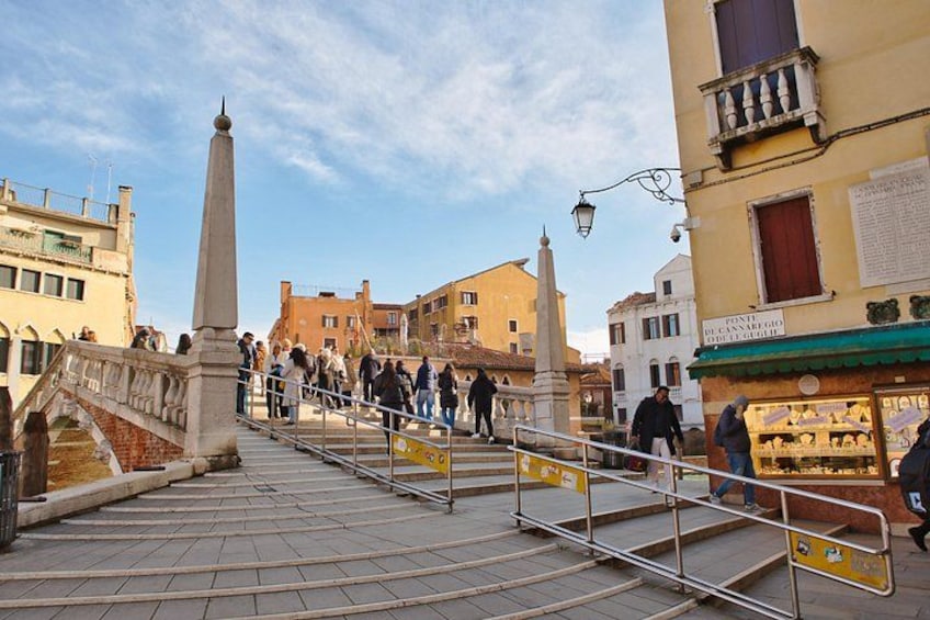 A pedestrian bridge with railings, a stone monument, and buildings in the background. 2