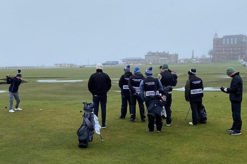 Eine Gruppe von Personen auf einem Golfplatz, im Hintergrund ein Gebäude. 5