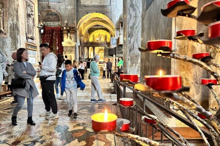 A church interior with red candles, marble columns, and people walking. 2