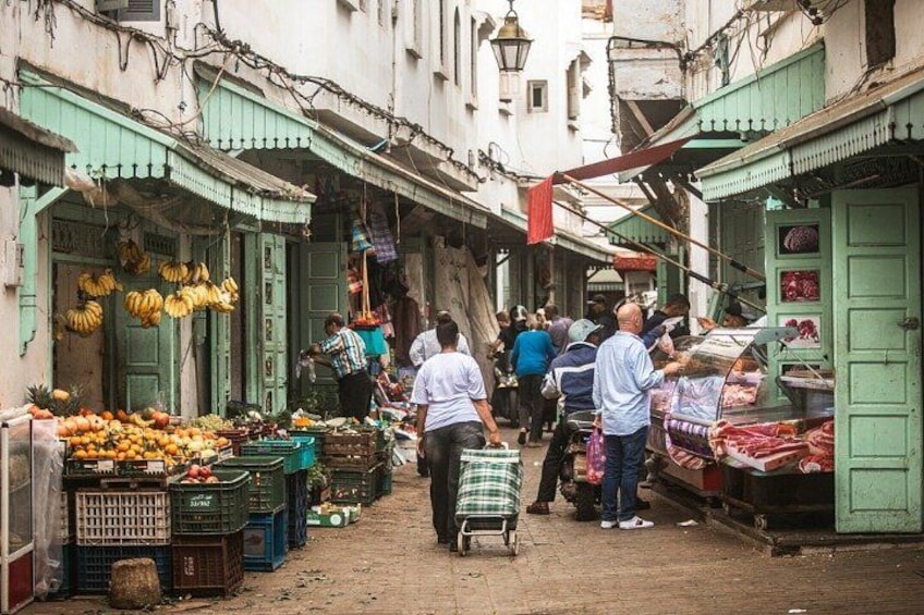 Una animada calle comercial con gente comprando y vendedores ofreciendo frutas y verduras. 4