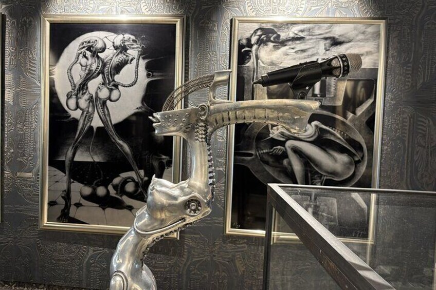 A sculpture of a gun in a gallery with two framed artworks on the wall. 1