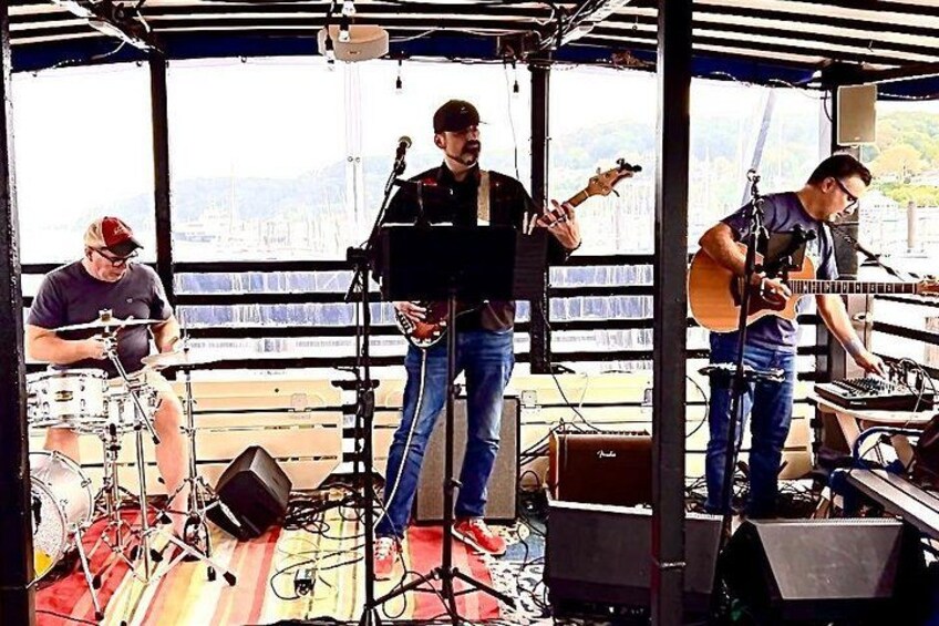 Ett band spelar på en båt med en stadsbild i bakgrunden. 4