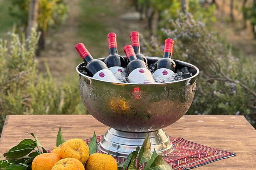 A metal bowl filled with wine bottles on a wooden table with oranges and leaves. 4