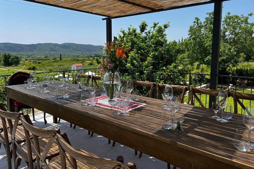 A wooden table set outdoors with wine glasses and a vase of flowers. 3